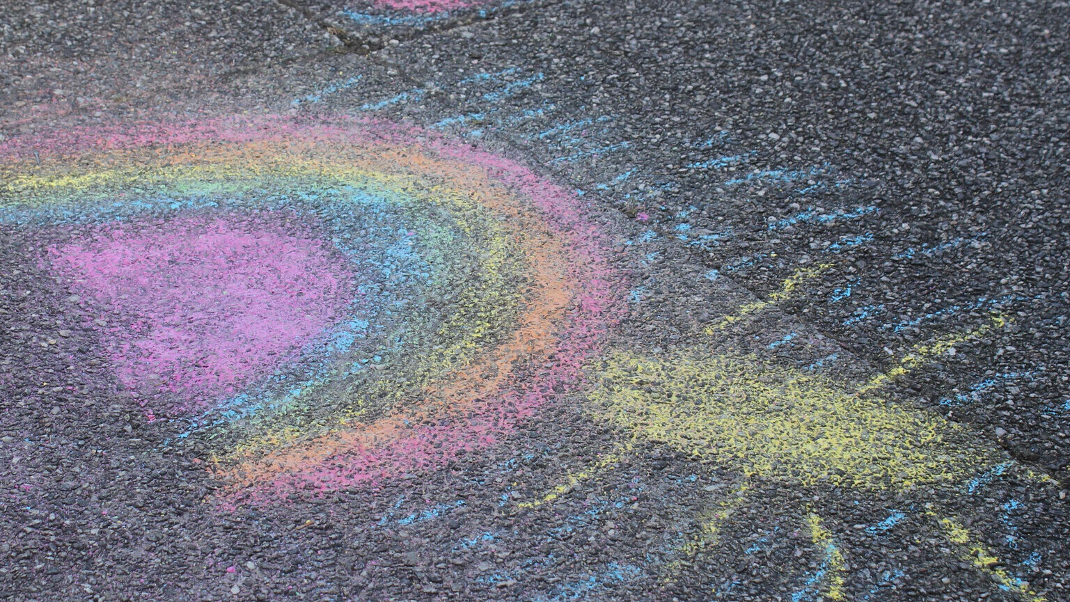 Ein Regenbogen und eine Sonne sind mit bunter Kreide auf eine Straße gemalt